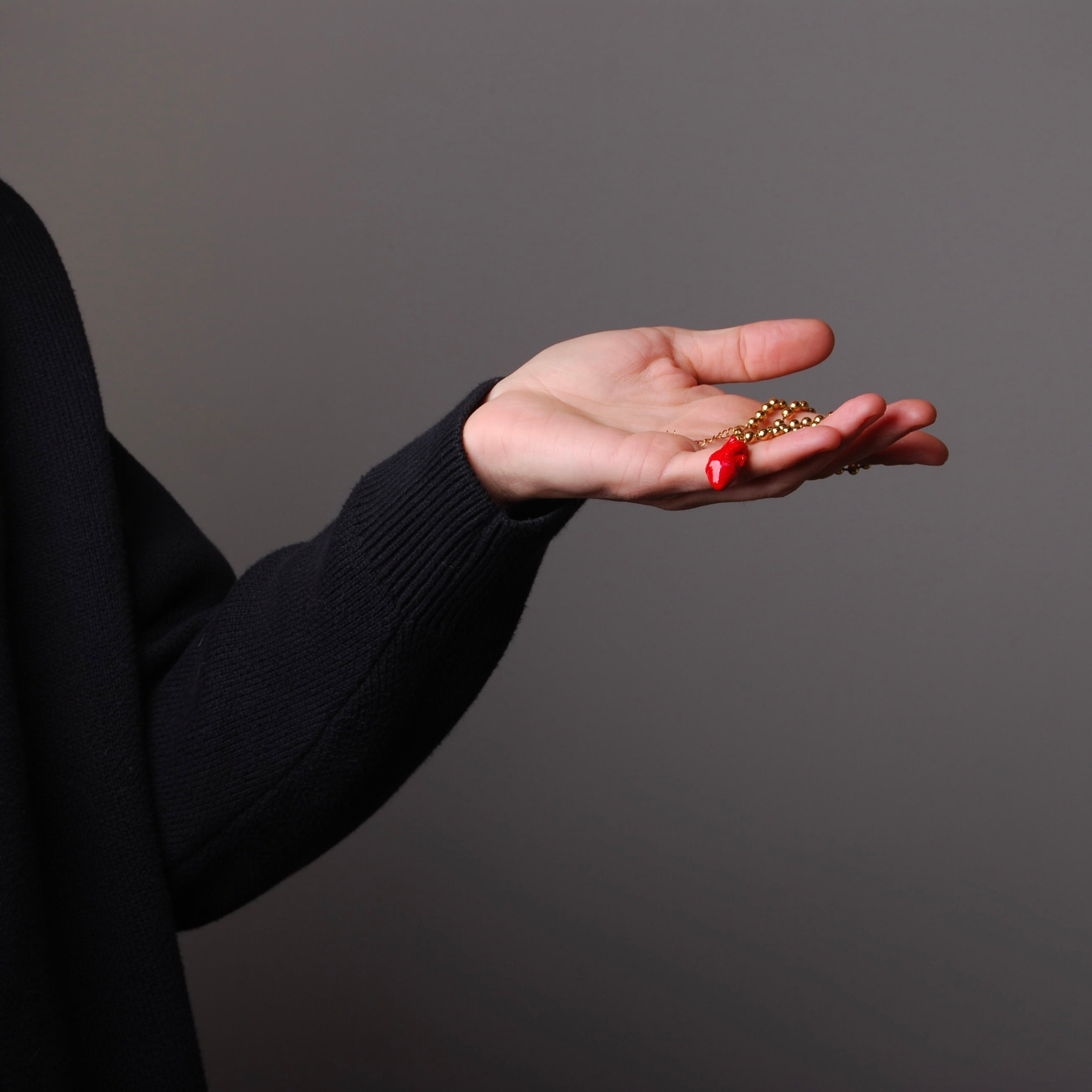 collana catena a sfere con pendente cuore anatomico rosso appoggiata su una mano