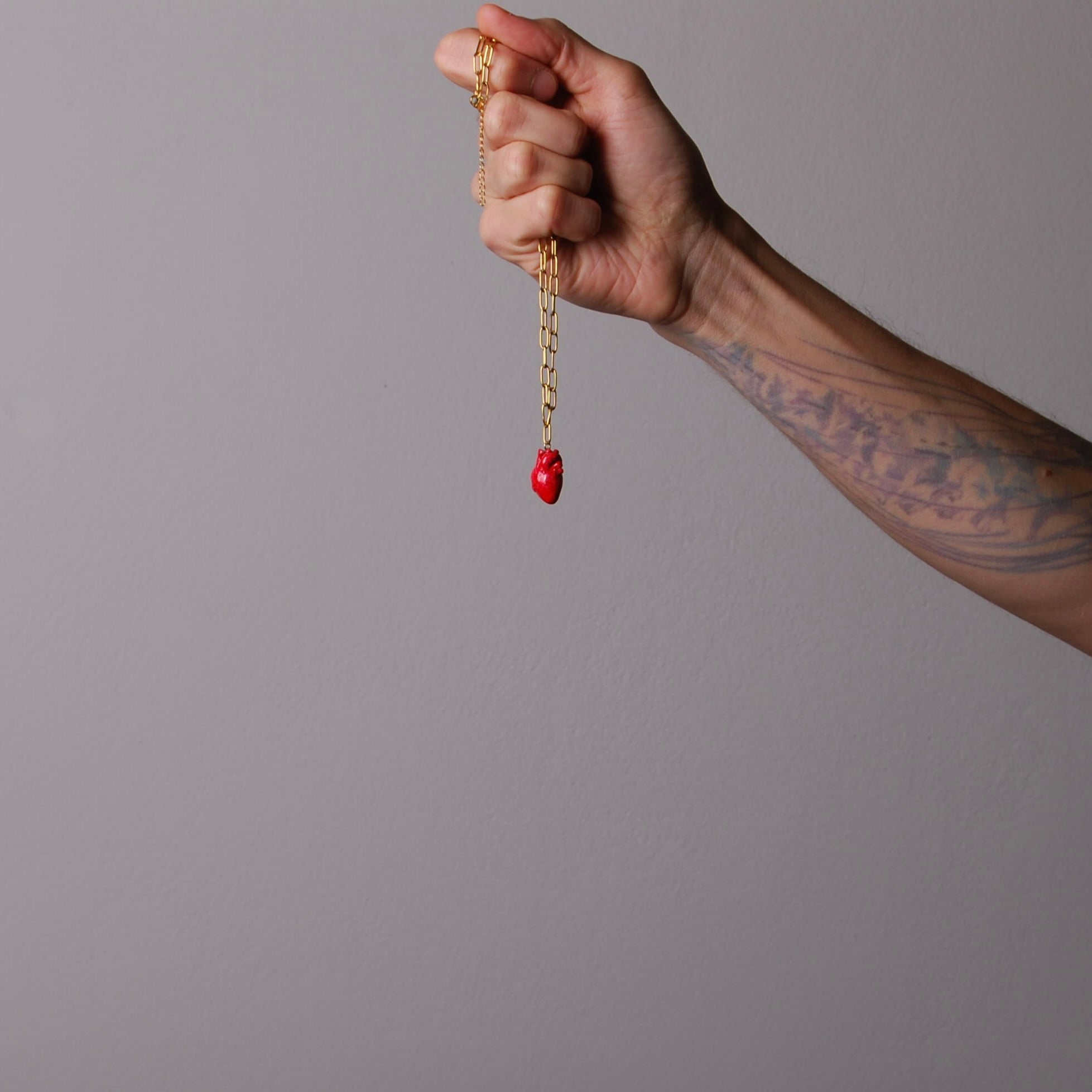mano che impugna una collana catena a maglia rettangolare con pendente cuore anatomico rosso
