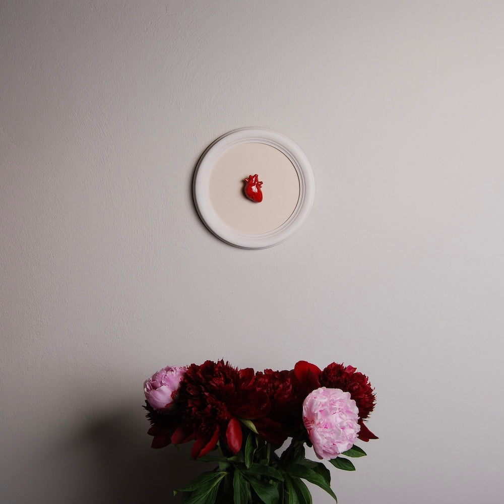 quadretto rotondo con cuore anatomico, appeso sopra peonie in vaso