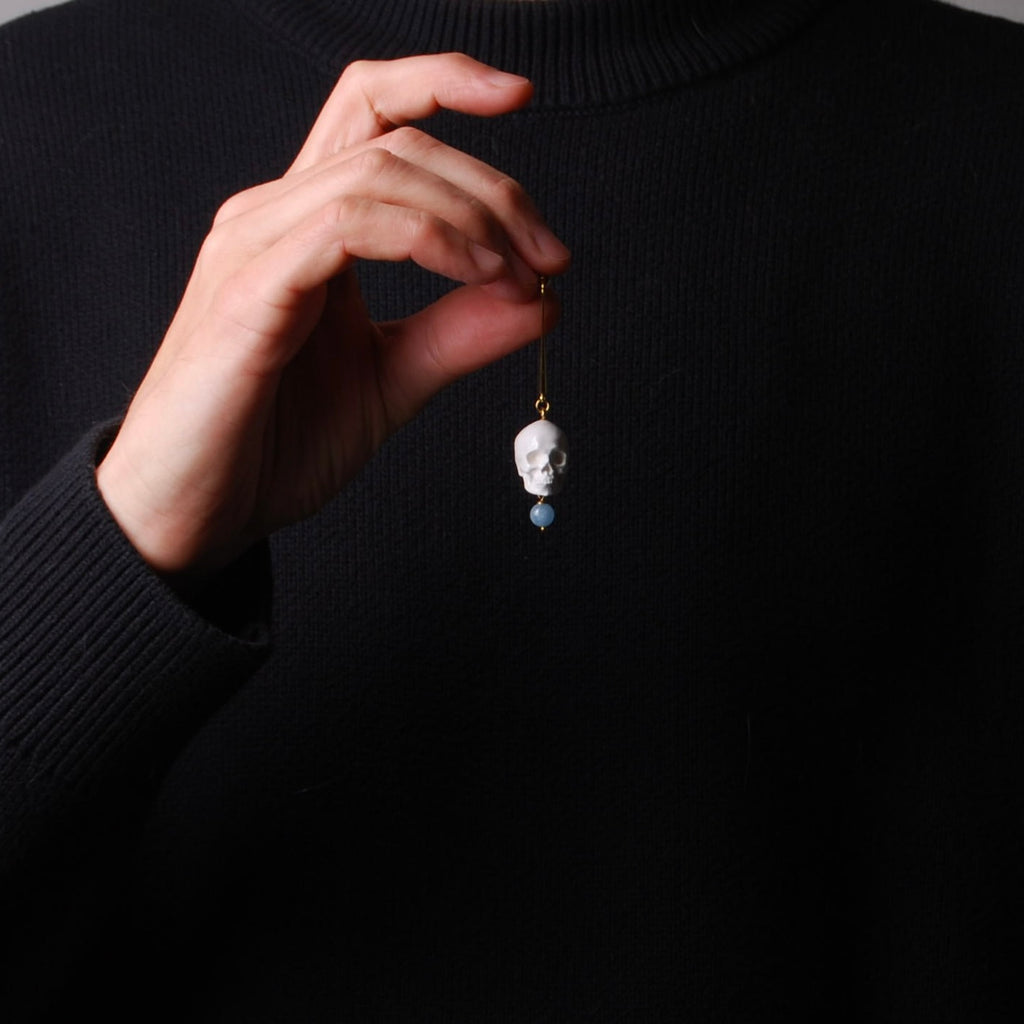 mano che tiene un orecchino con perno lungo e pendente teschio bianco e sfera di acquamarina