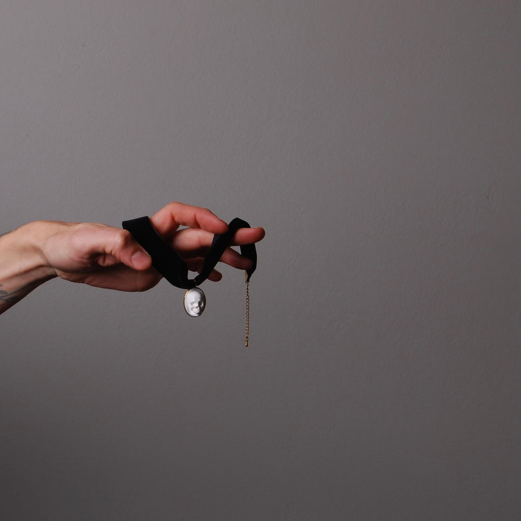 mano che tiene tra le dita un choker in velluto nero con pendente ovale con teschio bianco stile cammeo