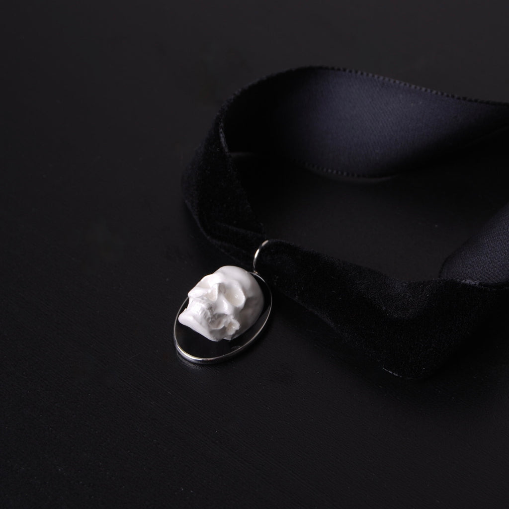 choker in velluto nero con pendente ovale con teschio stile cammeo, vista 3/4 dall'alto su piano nero