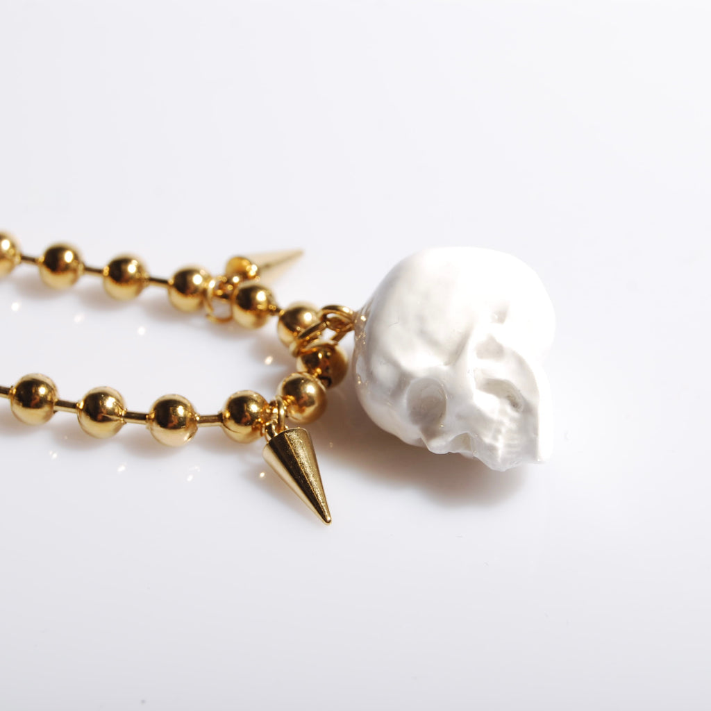 bracciale catena a sfere con pendente teschio bianco e punte, vista laterale del teschio appoggiato
