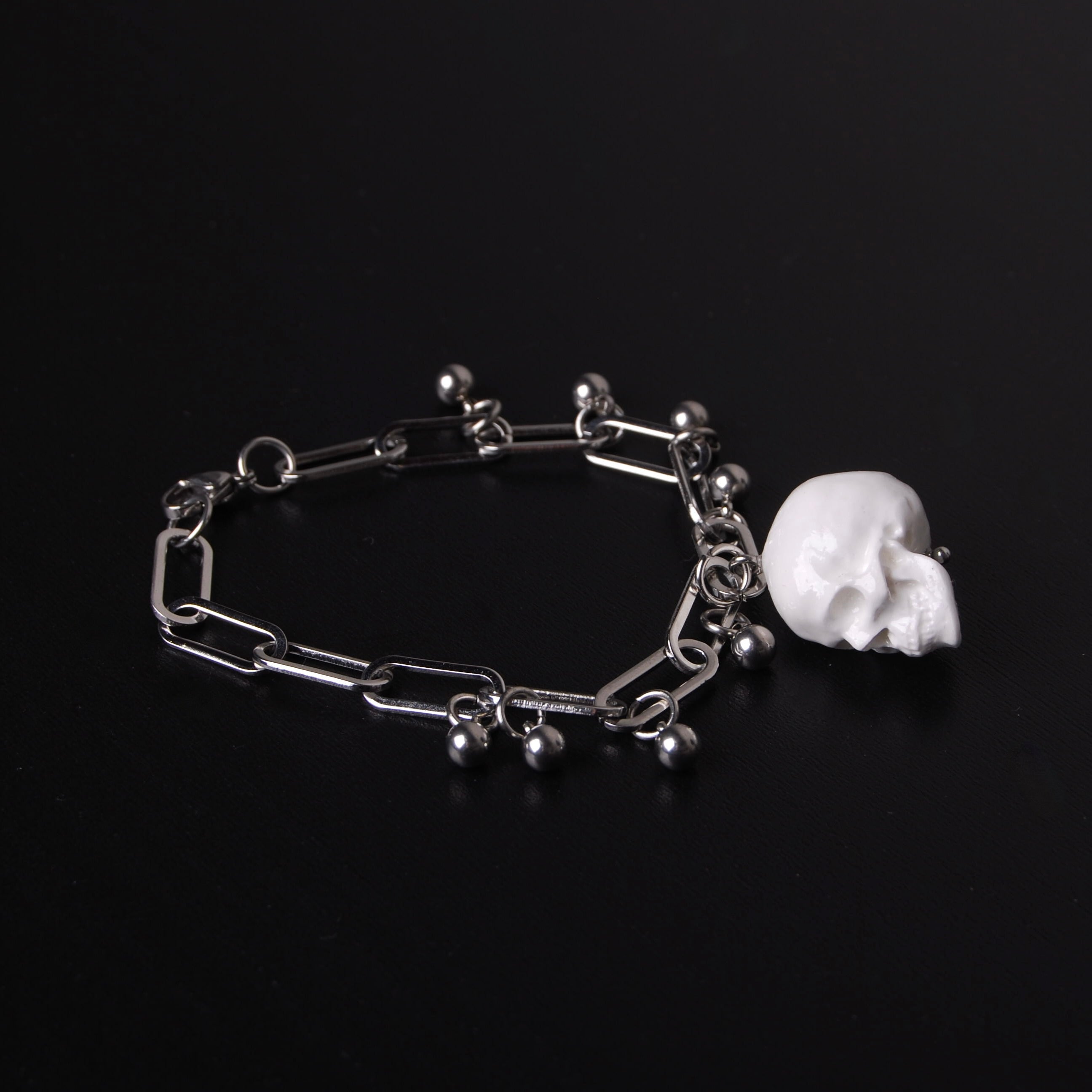 bracciale con pendente teschio bianco e sfere in acciaio, su fondo nero