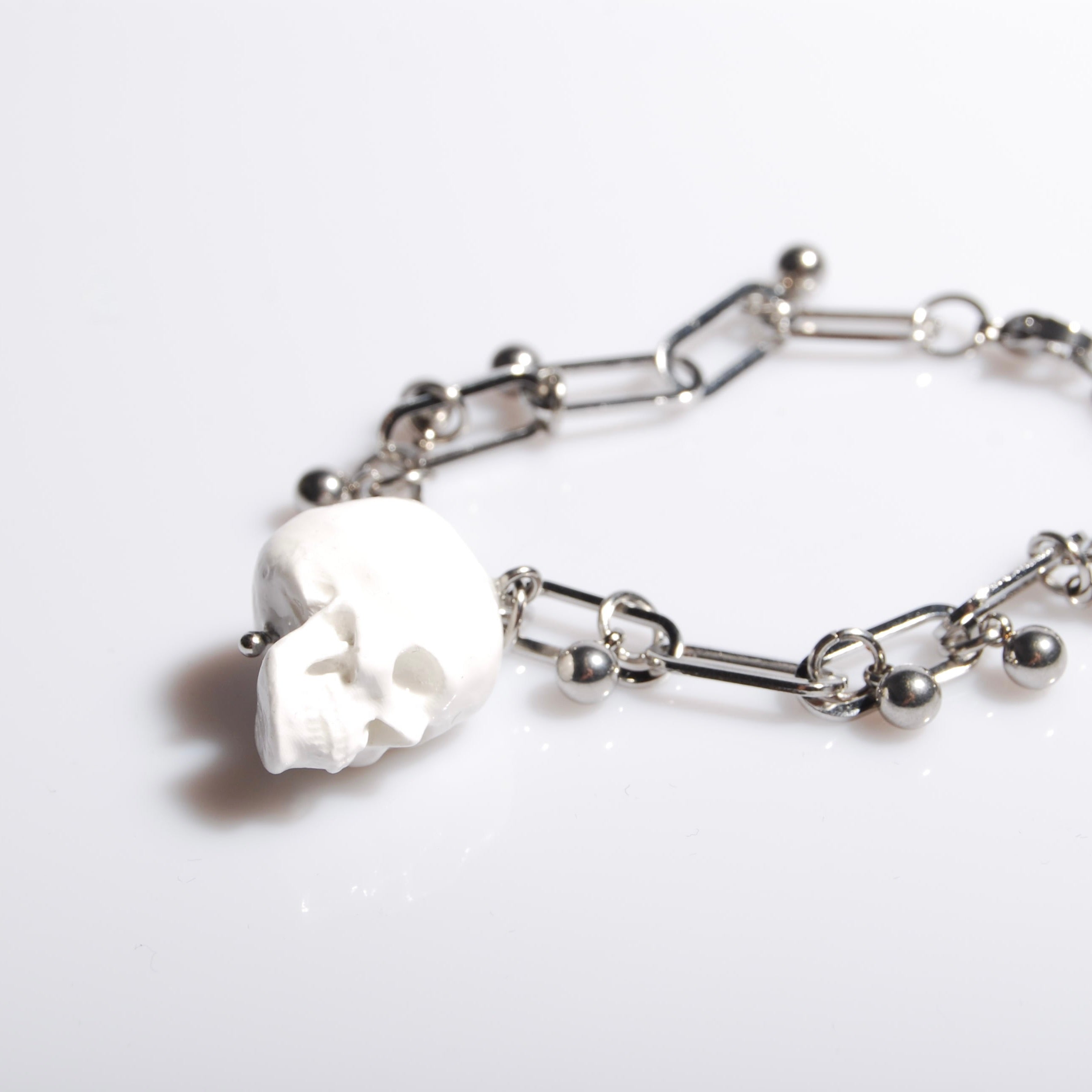 bracciale con pendente teschio bianco e sfere in acciaio, su fondo bianco