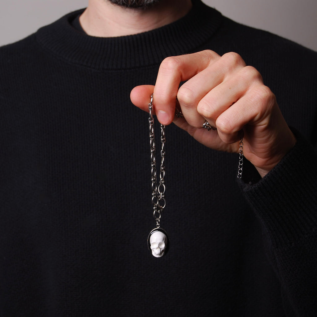 mano che tiene una collana a catena spessa con pendente ovale con teschio bianco stile cammeo