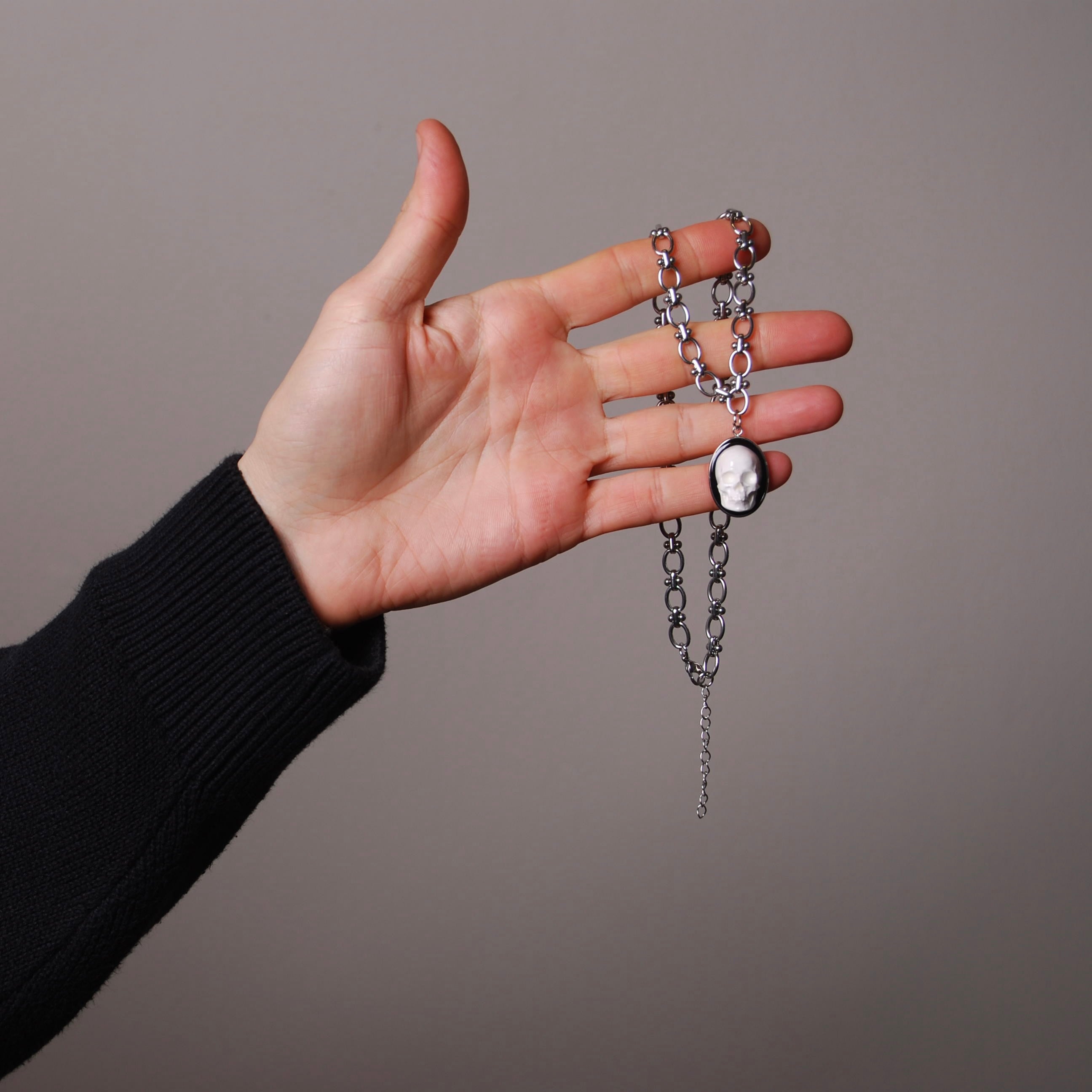 mano che tiene tra le dita una collana con catena spessa e pendente ovale con teschio bianco stile cammeo
