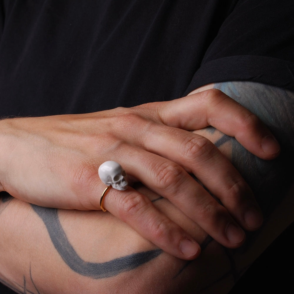 anello con teschio indossato su mano maschile, poggiata su braccio con tatuaggi