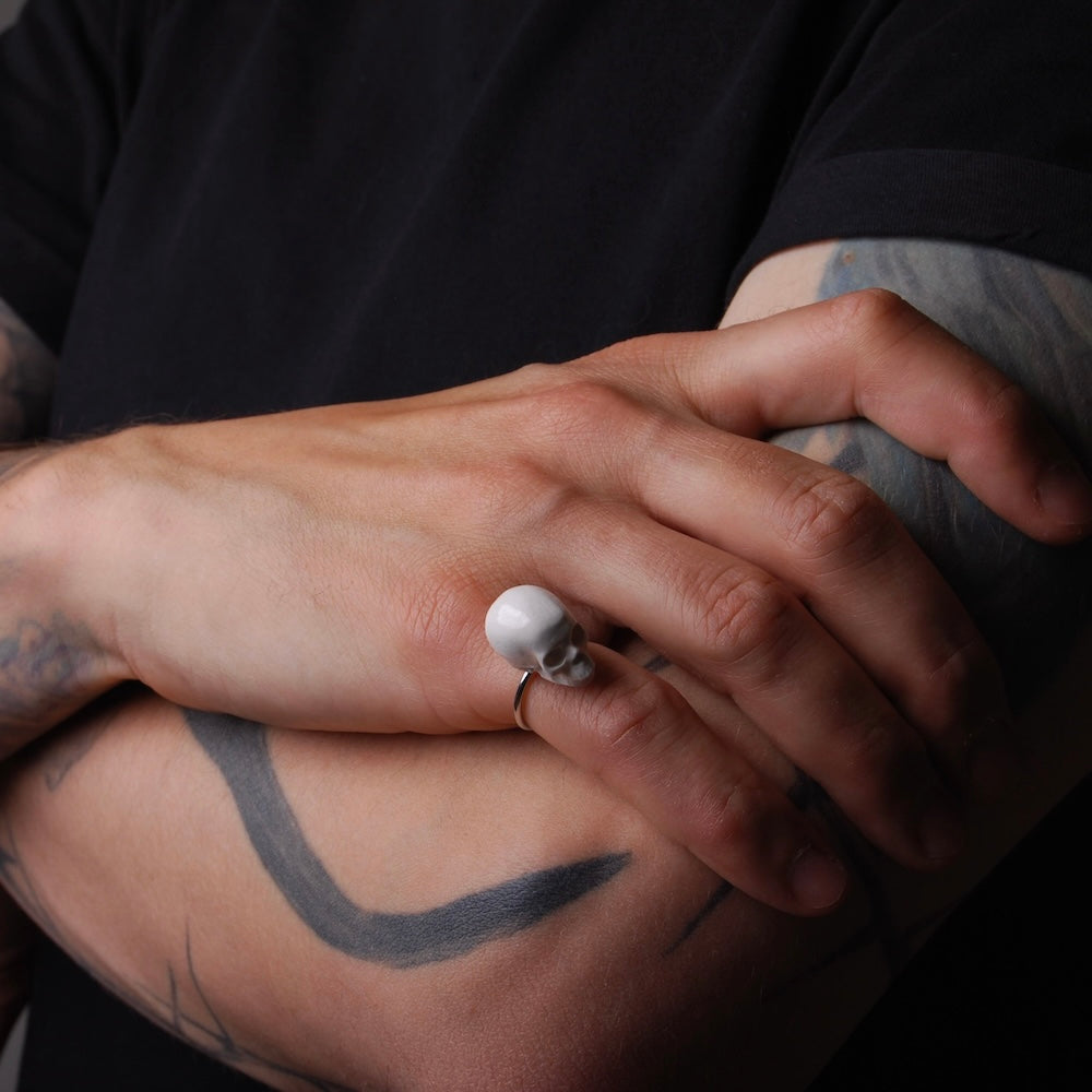 anello con teschio indossato su mano sottile, poggiata su braccio con tatuaggi