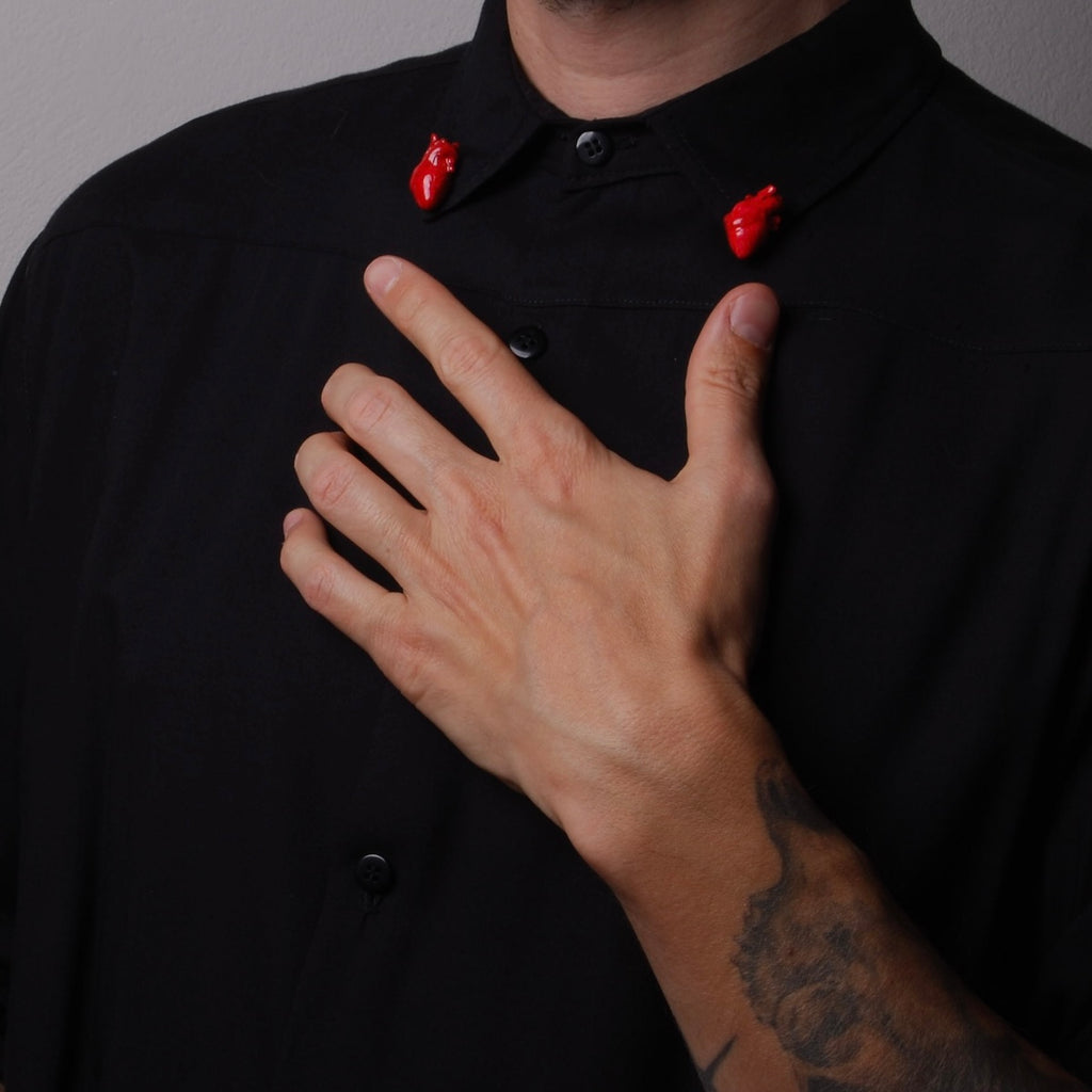 spillette a forma di cuore anatomico rosso indossate nel colletto di una camicia nera