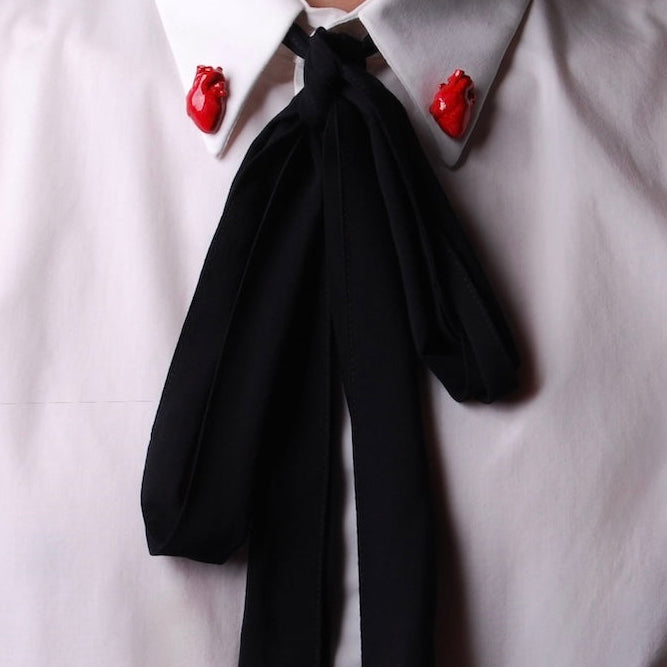 spillette cuore anatomico rosso indossate sul colletto di una camicia bianca con fiocco nero centrale morbido che cade