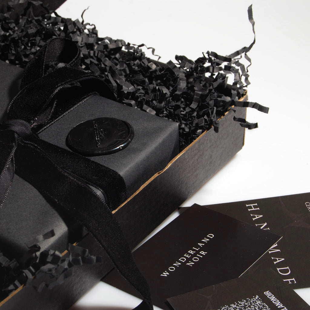 particolare del packaging nero con confezione regalo nera con nastro in velluto nero e sigillo in ceralacca con logo dentro una scatola nera con imbottitura in carta e bigliettini da visita