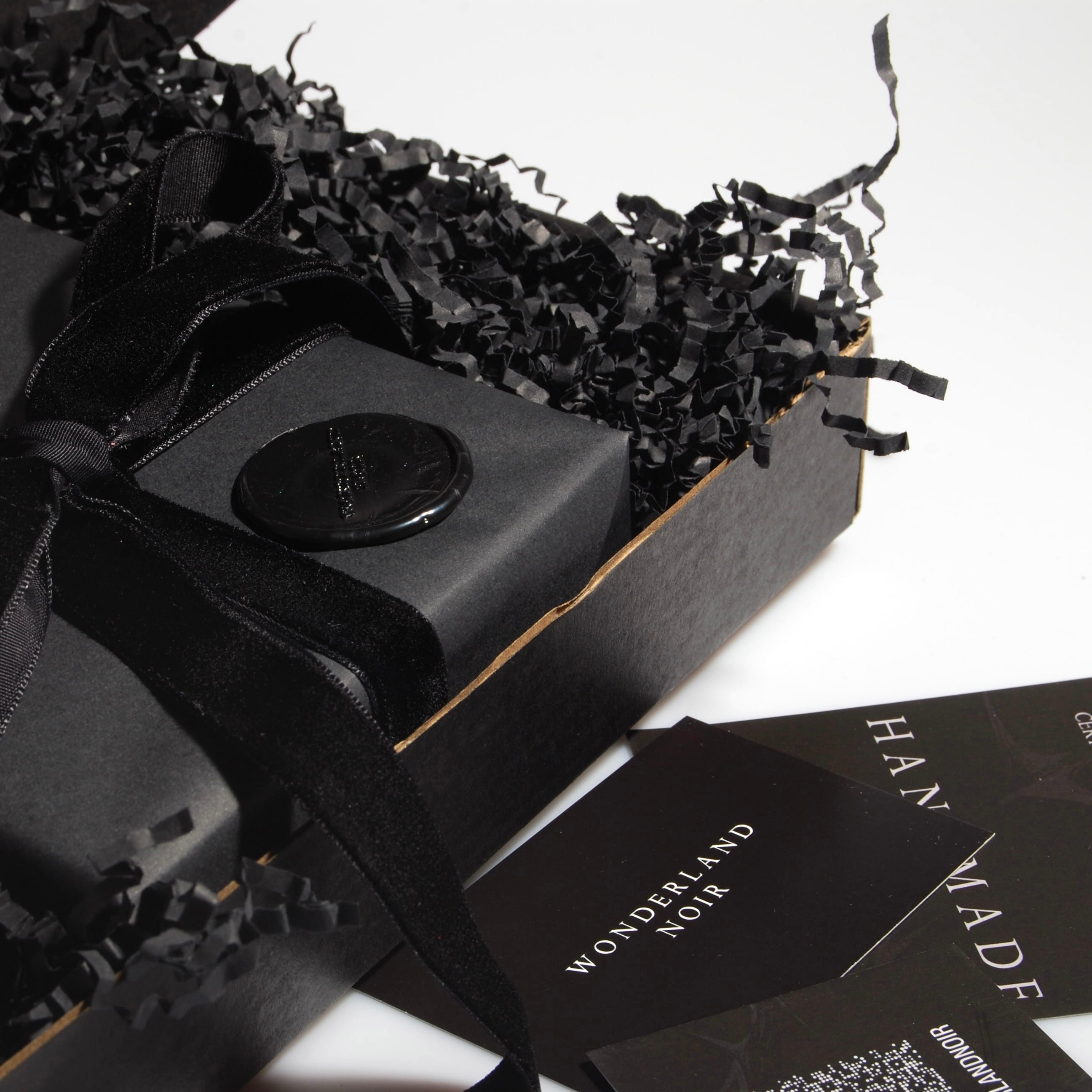 particolare del packaging nero con confezione regalo nera con nastro in velluto nero e sigillo in ceralacca con logo dentro una scatola nera con imbottitura in carta e bigliettini da visita