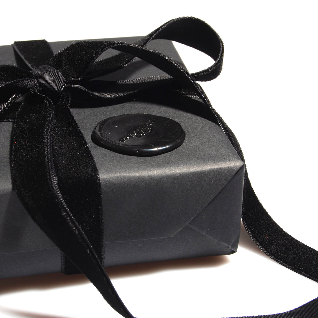 particolare di una confezione regalo nera con nastro in velluto nero e sigillo in ceralacca con logo
