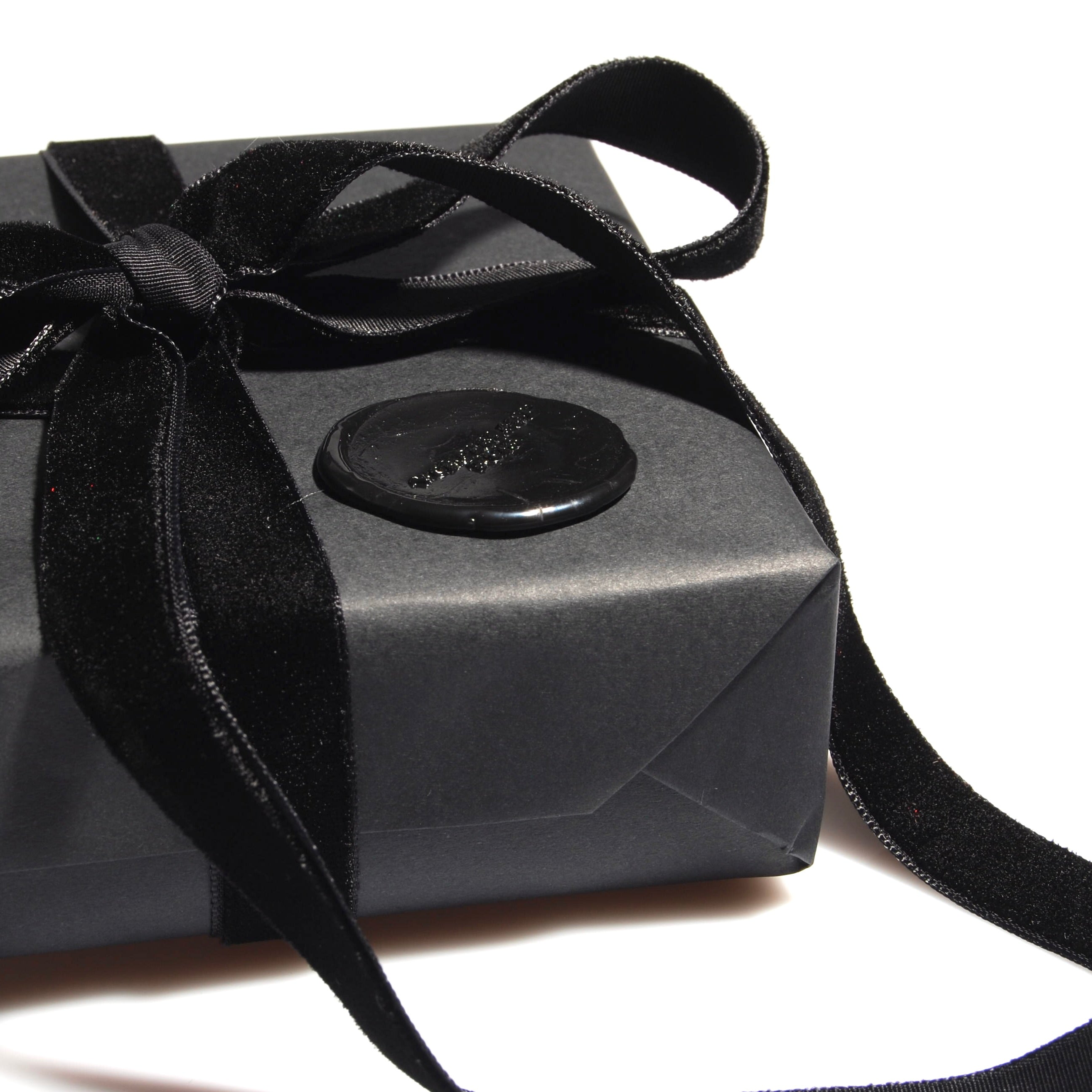 particolare di una confezione regalo nera con nastro in velluto nero e sigillo in ceralacca con logo