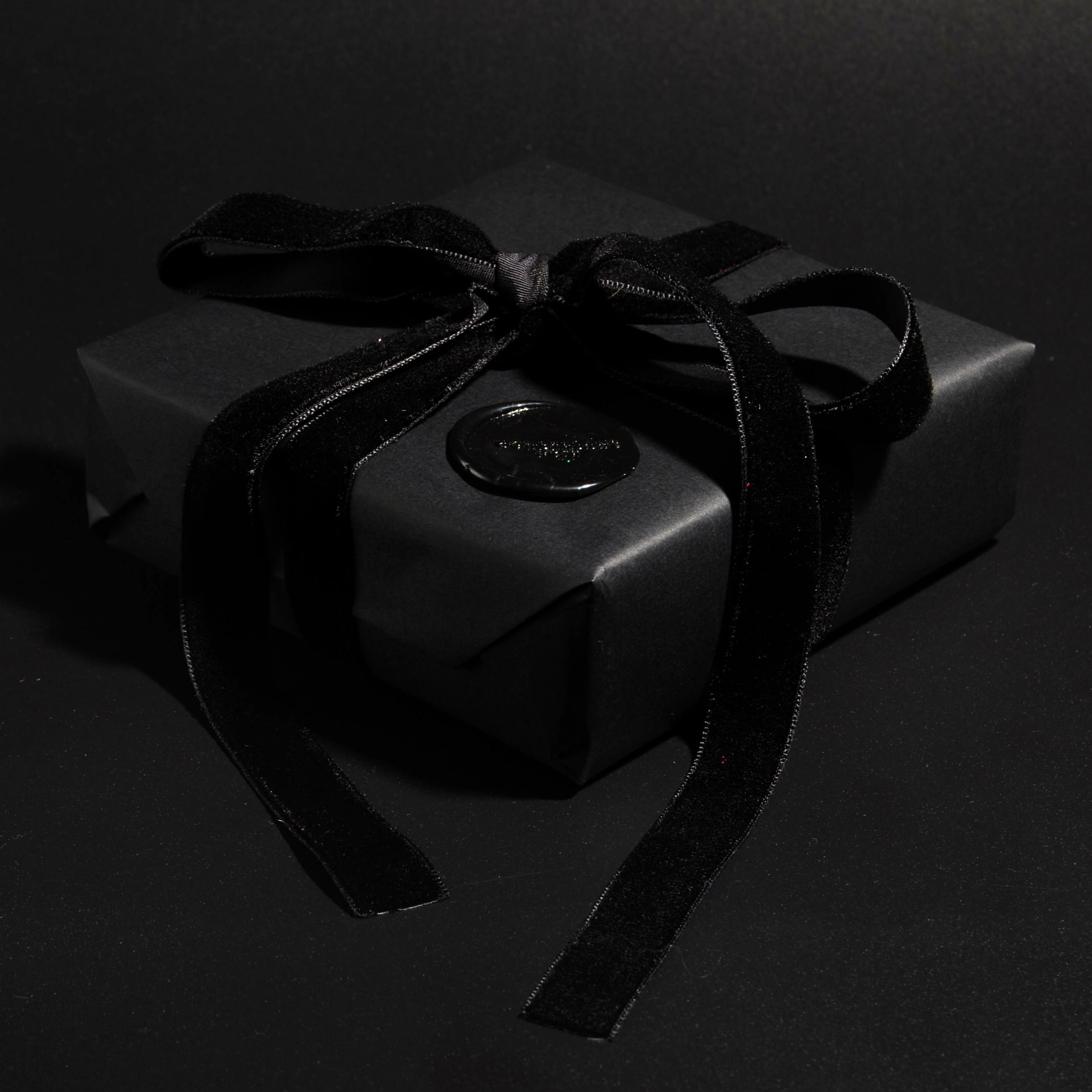 confezione regalo con carta nera e nastro nero, rifinita con sigillo in ceralacca, sfondo nero