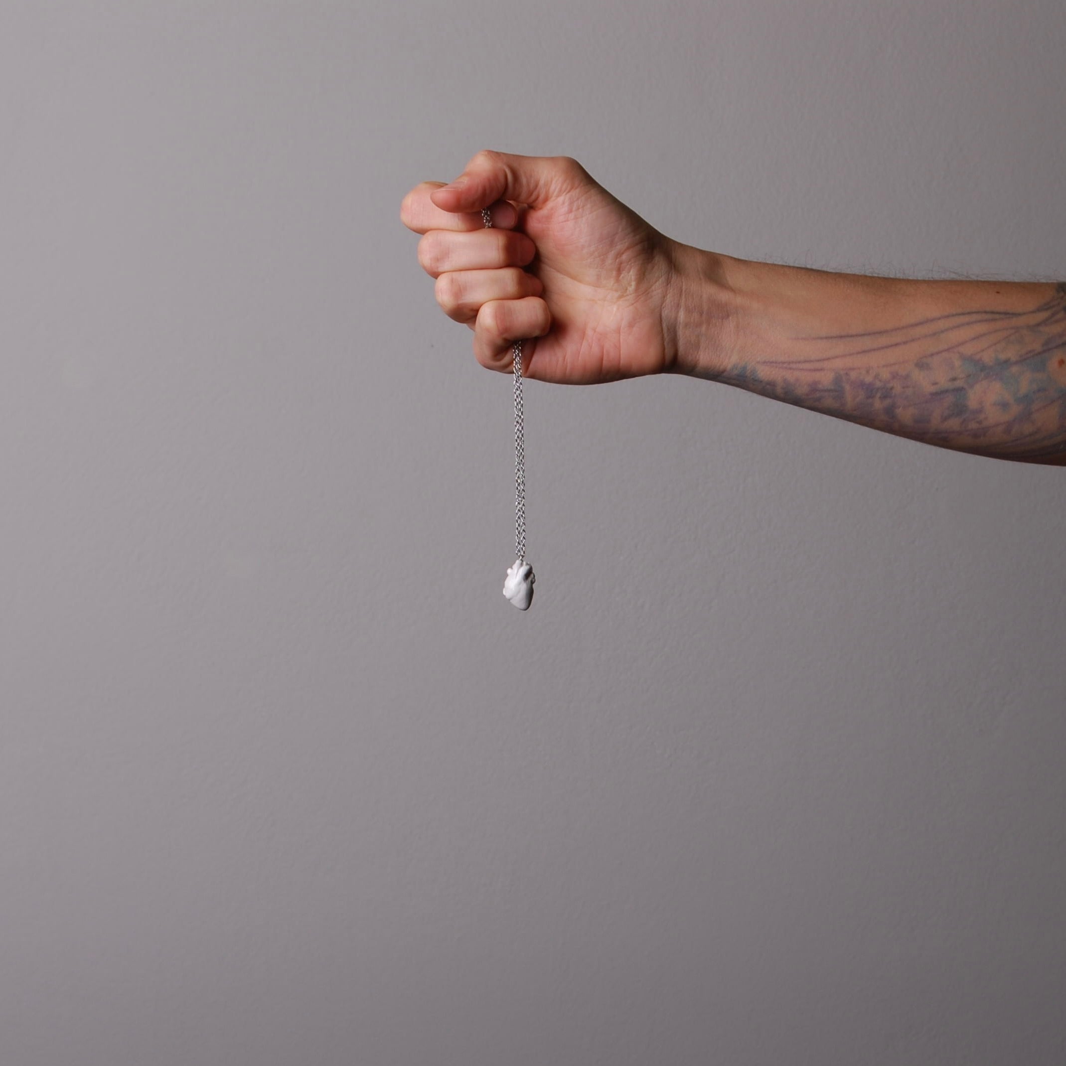 mano che impugna una collana a catena sottile con pendente cuore anatomico bianco