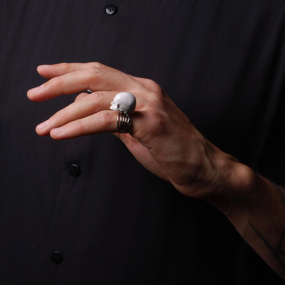 anello a base multipla con teschio bianco senza mandibola indossato sul mignolo di una mano
