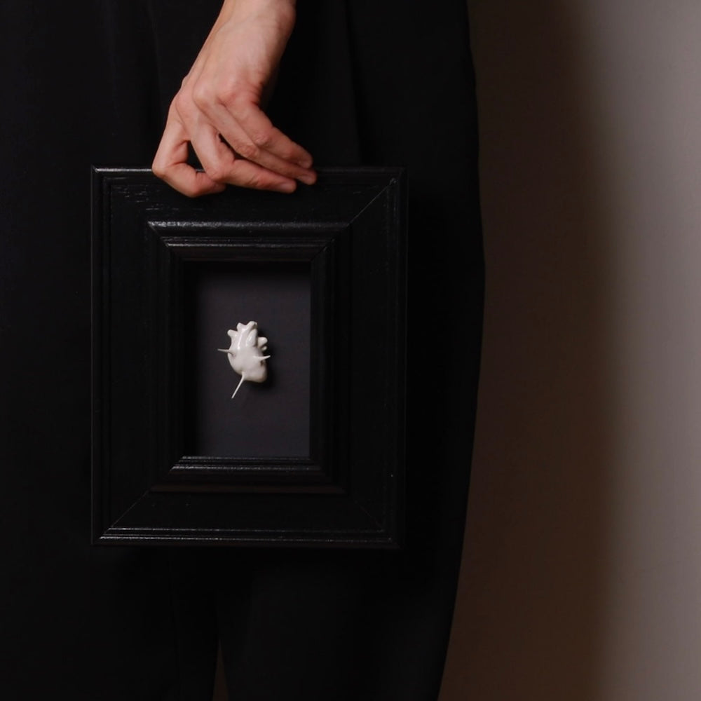 mano che sorregge un quadretto con miniatura cuore anatomico spinato bianco