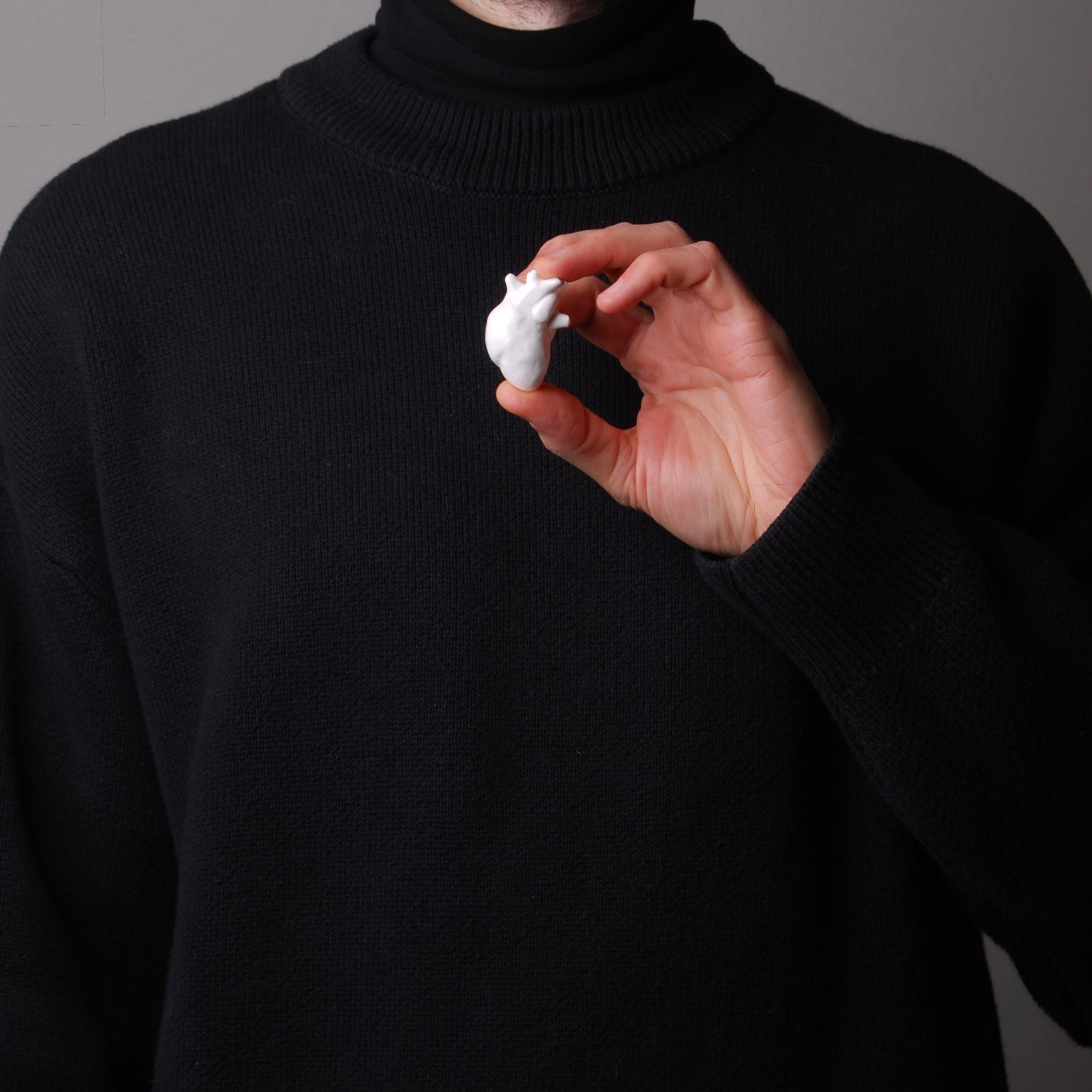 mano che tiene una spilla cuore anatomico bianco