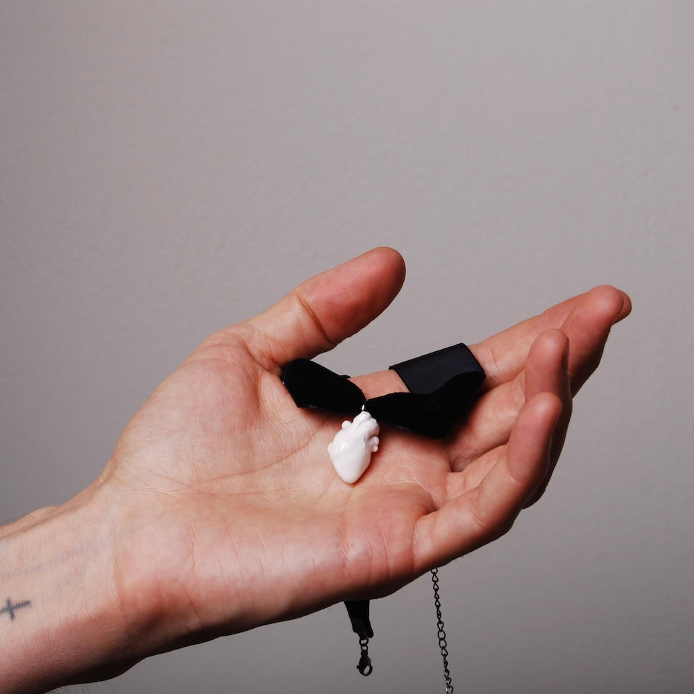 choker in velluto con pendente miniatura cuore anatomico bianco poggiato su una mano