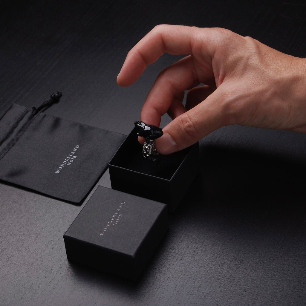 mano che posa un anello con cuore anatomico nero dentro ad una scatolina nera