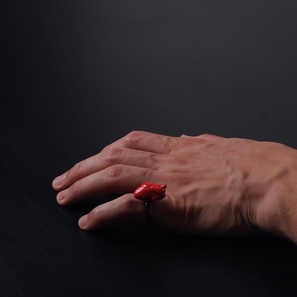 mano maschile che indossa sul mignolo un anello con cuore anatomico rosso