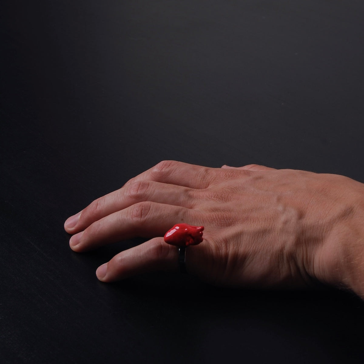 mano maschile che indossa sul mignolo un anello con cuore anatomico rosso