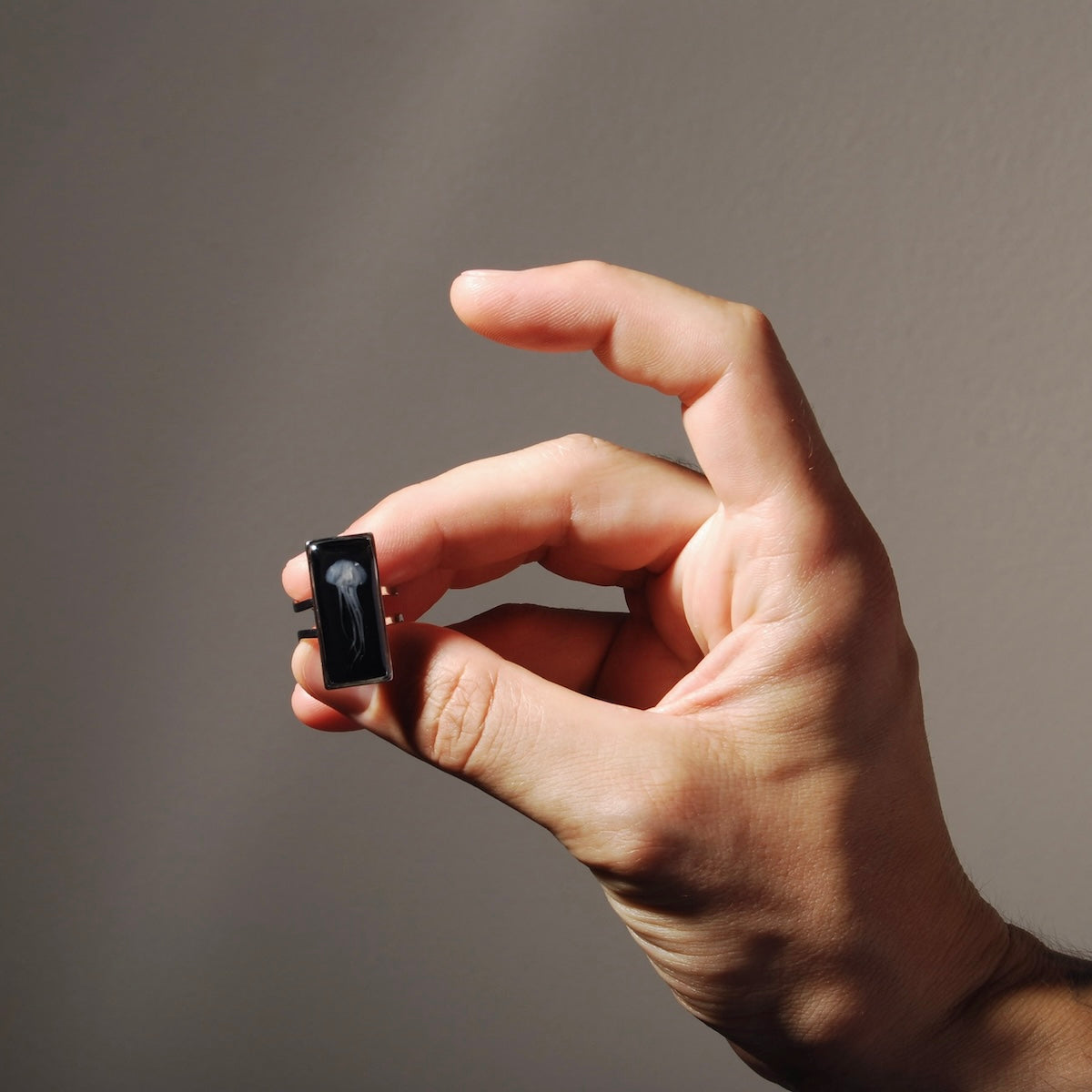 dita che tengono un anello rettangolare con medusa marina inglobata sotto resina
