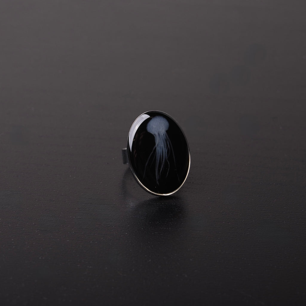 anello ovale con medusa marina inglobata sotto resina, vista frontale su piano nero