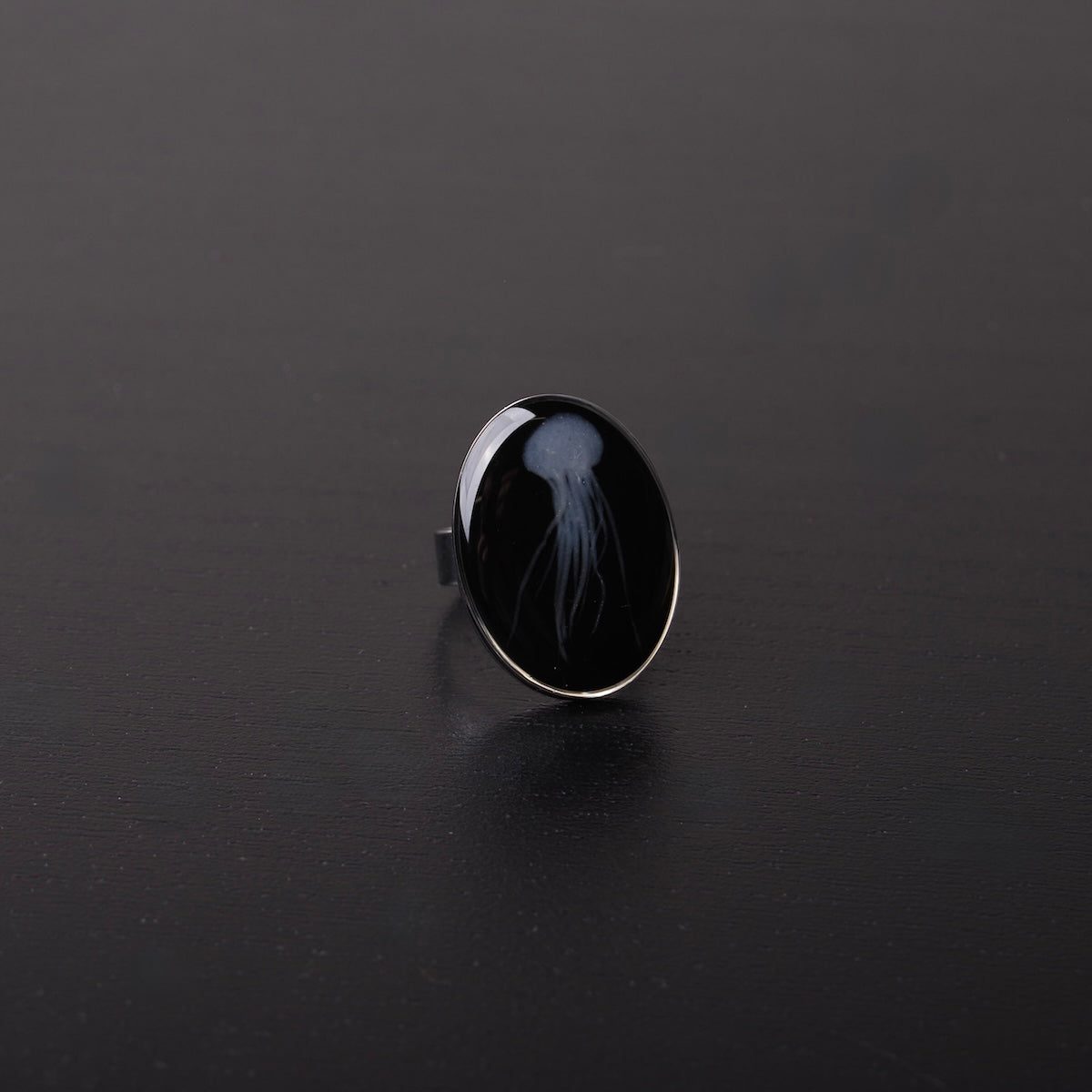 anello ovale con medusa marina inglobata sotto resina, vista frontale su piano nero