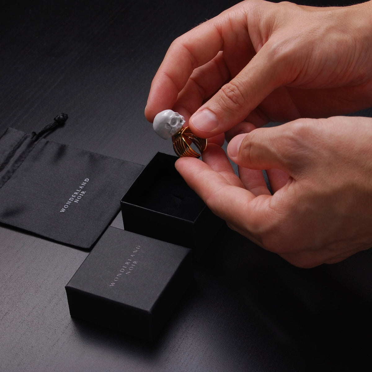 mani che poggiano un anello a banda larga con teschio grigio dentro ad una scatolina nera