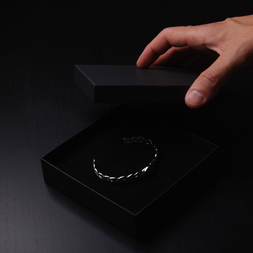 mano che chiude una scatolina nell'ombra, contenente un bracciale rigido intrecciato con ovale centrale con medusa marina inglobata sotto resina