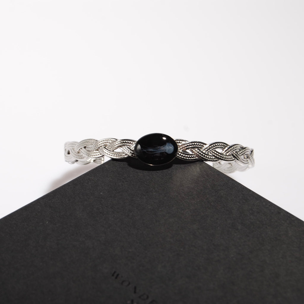 bracciale rigido intrecciato con ovale centrale con medusa marina inglobata sotto resina poggiato su una scatolina nera