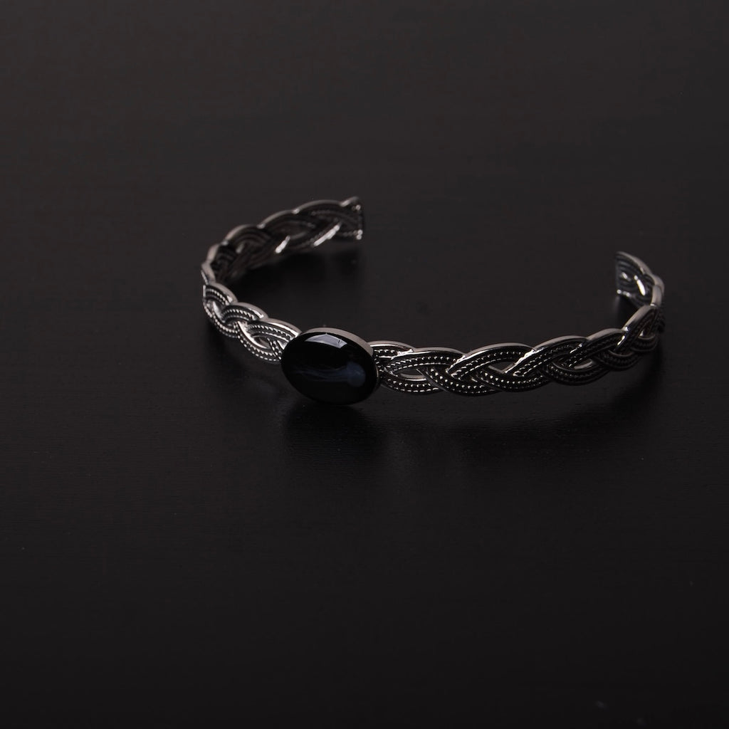 bracciale rigido intrecciato con ovale centrale con medusa marina inglobata sotto resina poggiato su ripiano nero