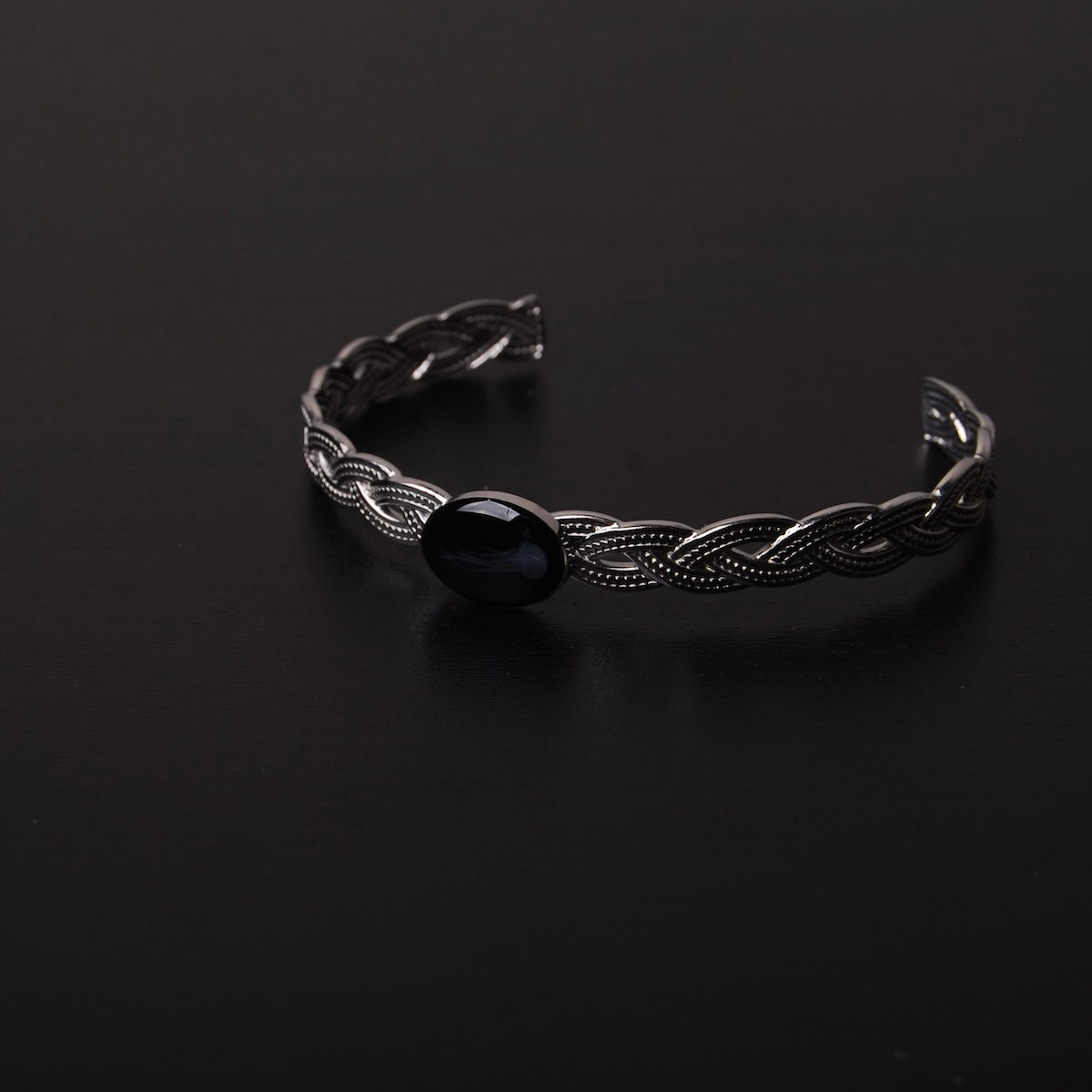 bracciale rigido intrecciato con ovale centrale con medusa marina inglobata sotto resina poggiato su ripiano nero