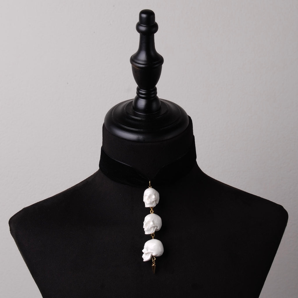 choker in velluto nero con fila di teschi e punta in acciaio placcato oro su busto espositivo in velluto