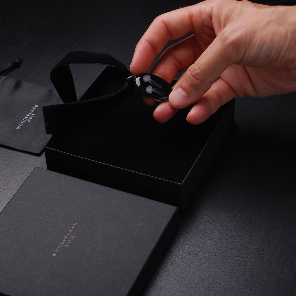 mano che posa un choker in velluto nero con pendente ovale con meduse marine in una scatola nera
