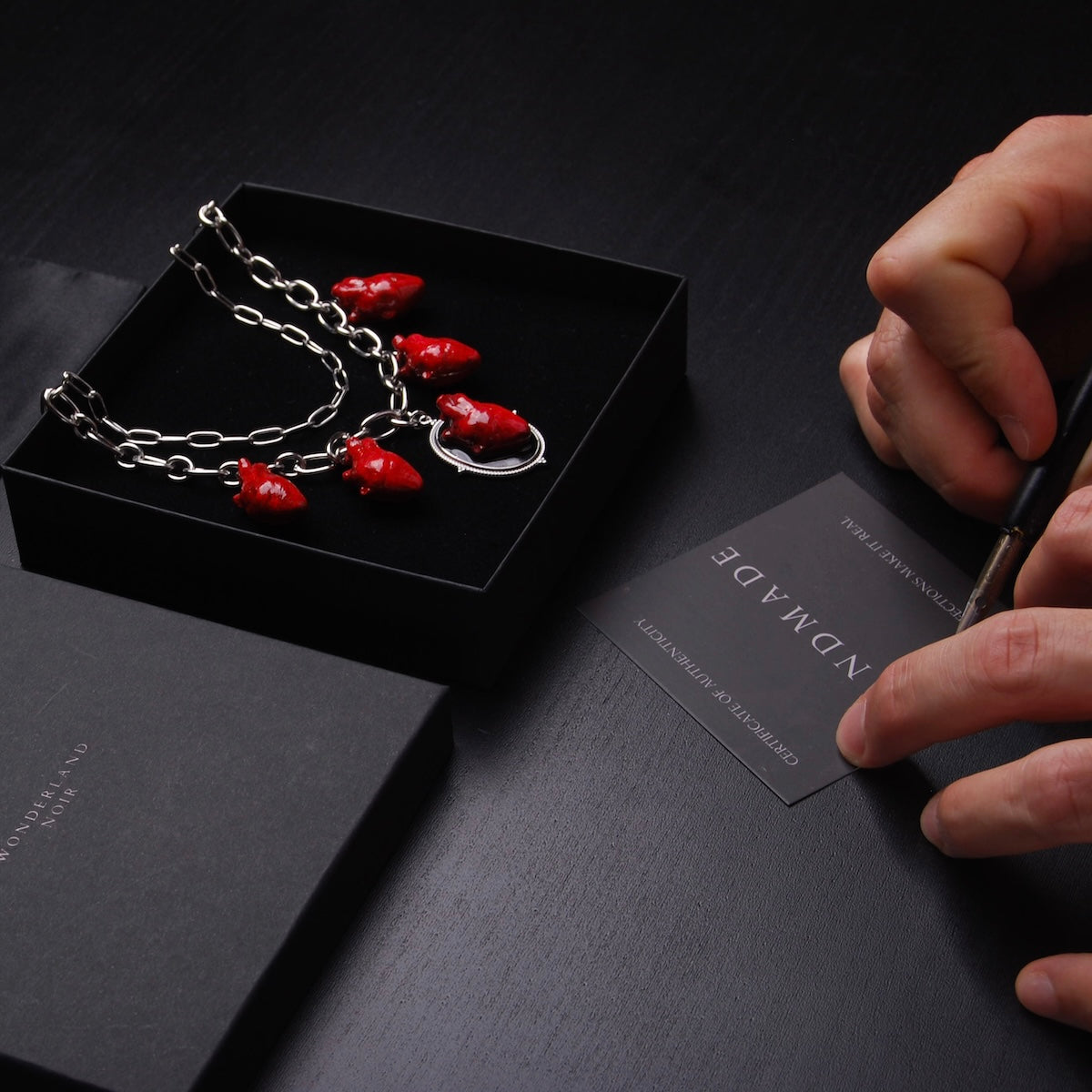 collana a catena doppia con 5 cuori anatomici pendenti dentro ad una scatolina con mani che firmano un certificato di autenticità