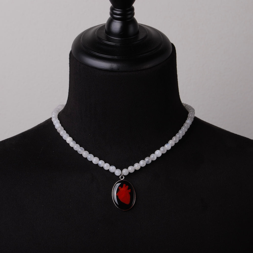 collana con sfere di pietra di luna e pendente centrale ovale con cuore anatomico su busto espositivo, vista frontale