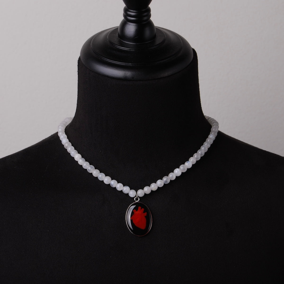 collana con sfere di pietra di luna e pendente centrale ovale con cuore anatomico su busto espositivo, vista frontale