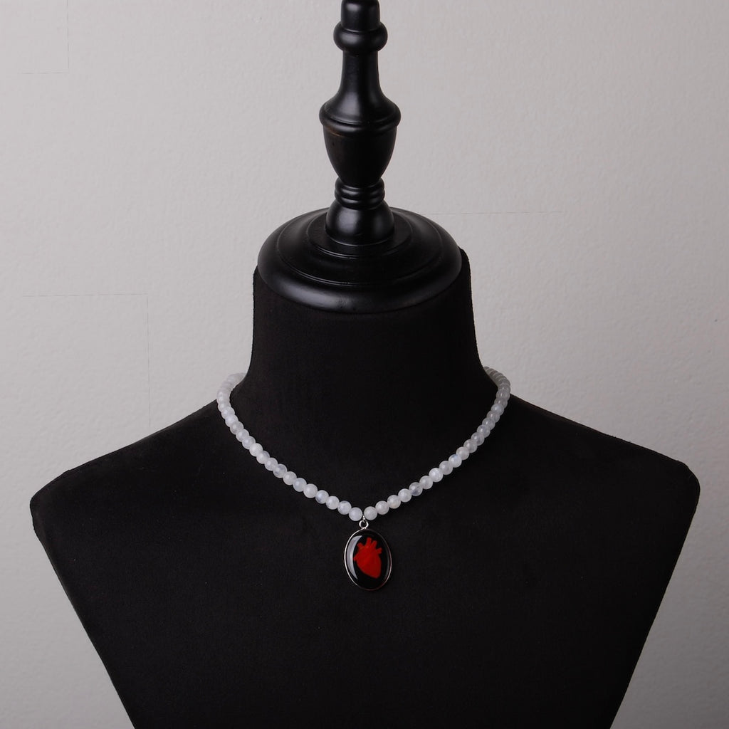 collana con sfere di pietra di luna e pendente centrale ovale con cuore anatomico su busto espositivo