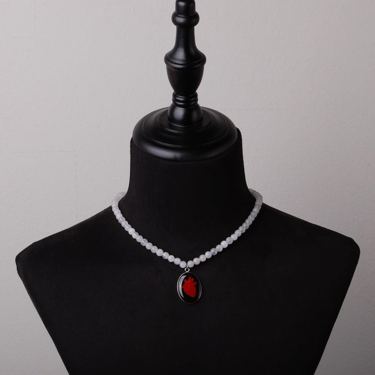 collana con sfere di pietra di luna e pendente centrale ovale con cuore anatomico su busto espositivo