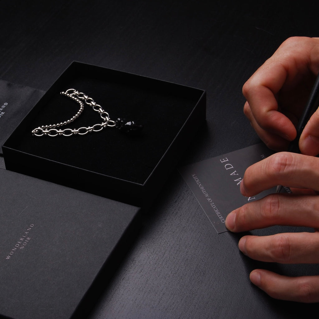 collana catena doppia con cuore anatomico nero dentro ad una scatolina, con mani che firmano un certificato di autenticità
