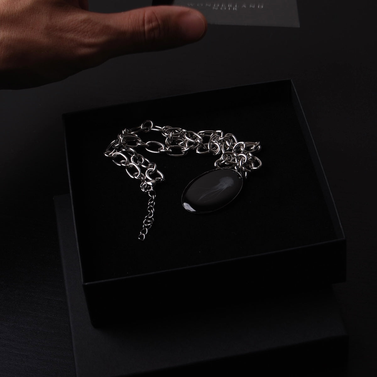 mano che chiude una scatolina con collana con pendente ovale con medusa marina