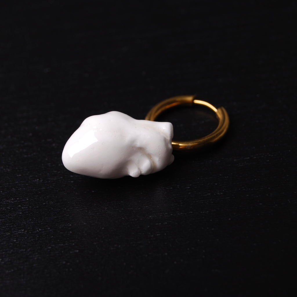 orecchino cuore anatomico bianco su cerchio in acciaio dorato poggiato su un piano nero