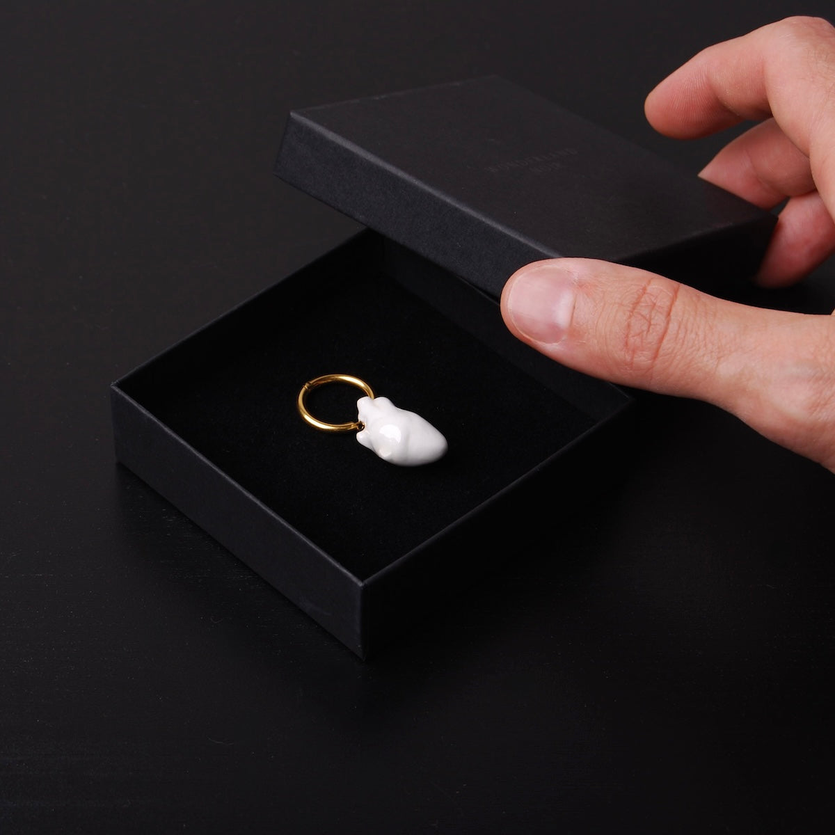 mano che chiude una scatolina con un orecchino singolo con pendente cuore anatomico bianco
