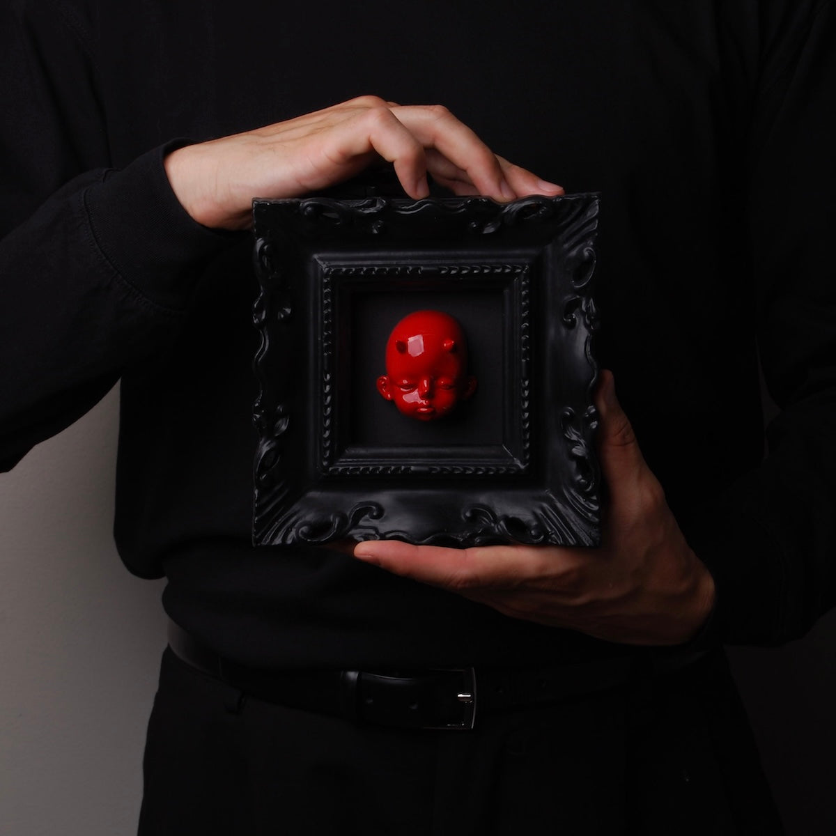 mani che tengono un quadretto barocco nero con testa di diavoletto rosso