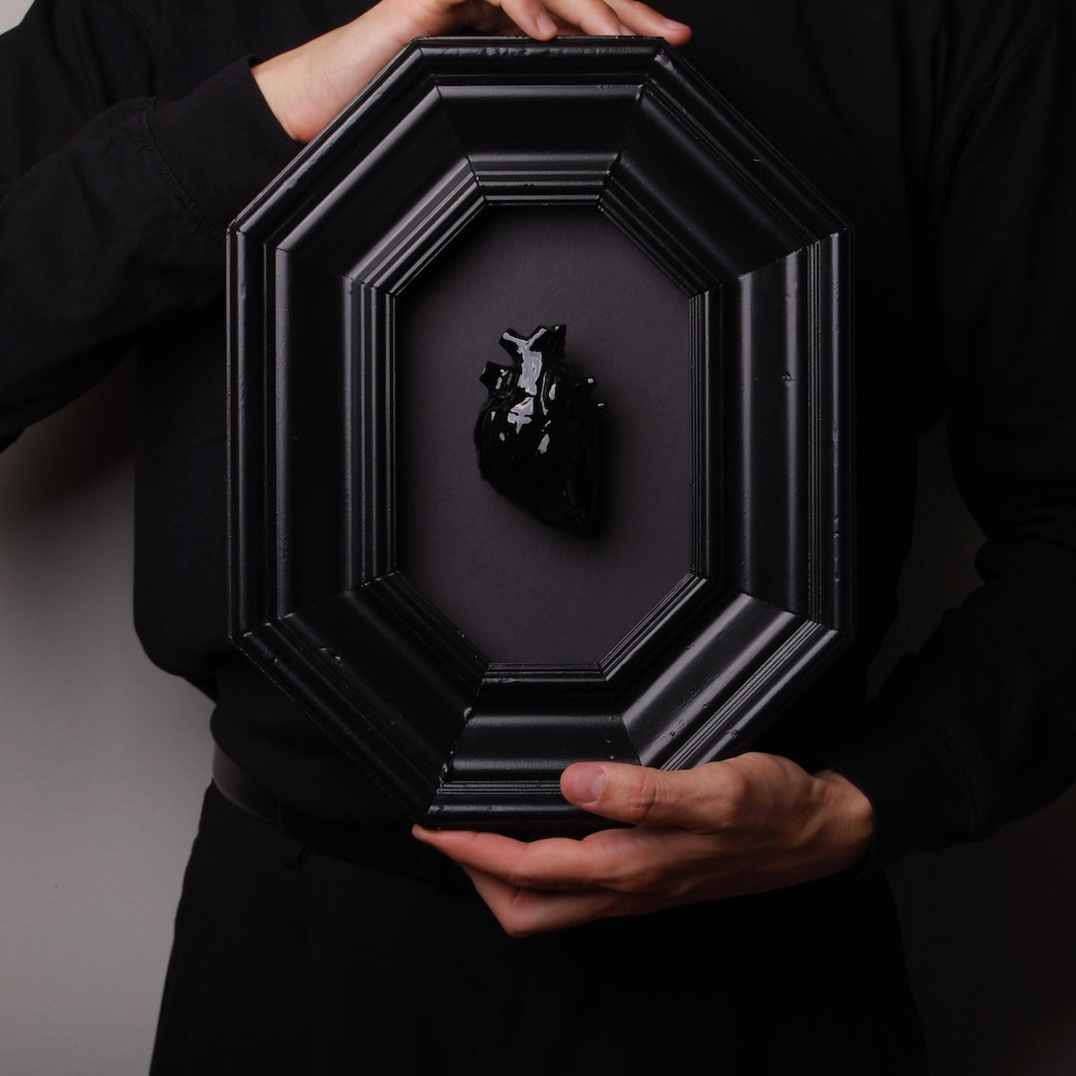 mani che tengono un quadro cornice ottagonale con cuore anatomico nero