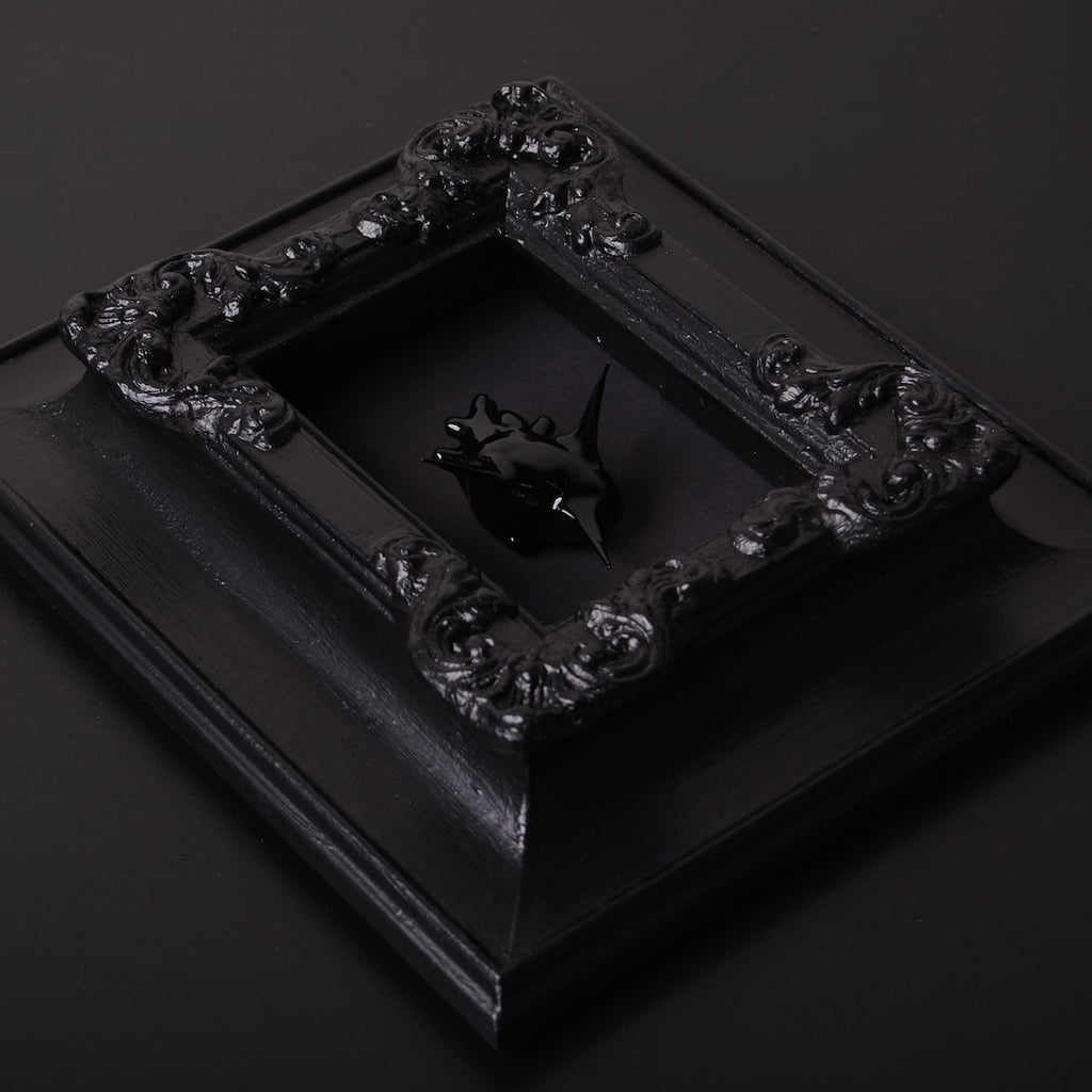 un quadro con cornice antica con cuore anatomico spinato nero, vista 3/4
